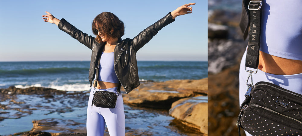 Carefree model walking by ocean while wearing the Aimee Kestenberg Nylon Camera Crossbody in Microstuds.